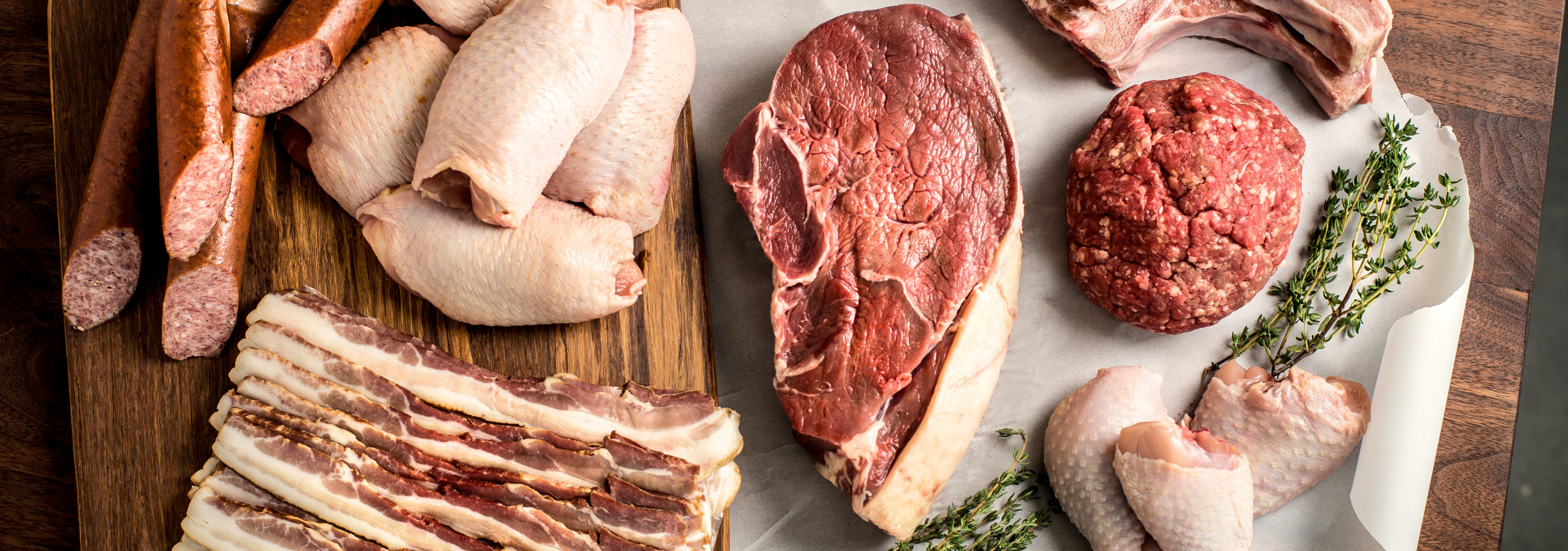 Assorted meats including sausages, bacon, and ground beef on a wooden cutting board.